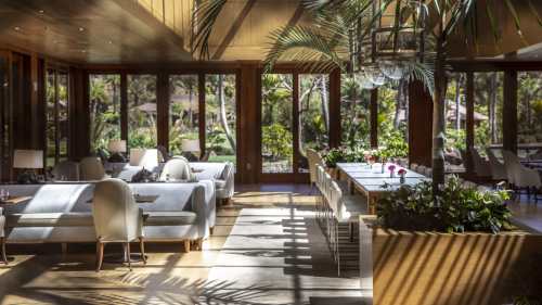 Bright, modern restaurant interior with large windows, lush greenery, and elegant seating arrangements.