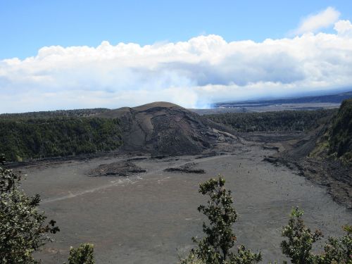 A panoramic view of a volcanic landscape with a crater, surrounded by trees and a cloudy sky in the background.