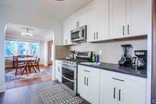 Modern kitchen with stainless steel appliances, white cabinets, and a dining area visible through an archway.
