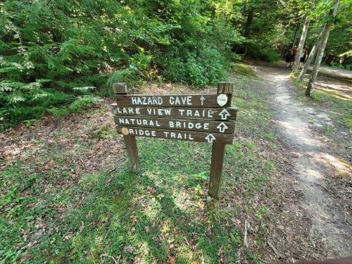 Wooden signpost with trail directions: Hazard Cave, Lake View Trail, Natural Bridge, and Ridge Trail in a forested area.