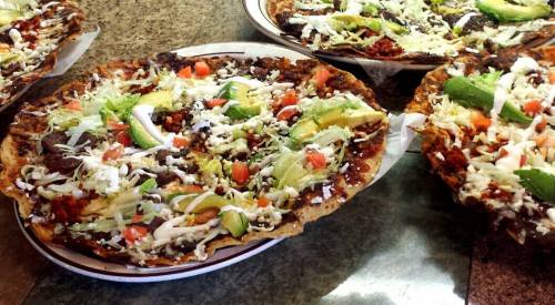 A close-up of colorful, loaded tacos on a plate, topped with lettuce, tomatoes, avocado, and sour cream.