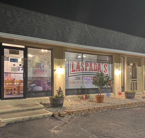 Exterior of Laspada's Pizzeria at night, featuring a sign and decorative planters with flowers and pinwheels.