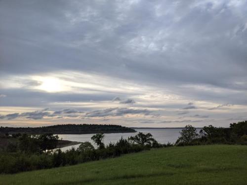 A serene landscape featuring a calm lake, green grass, and a cloudy sky at sunset.
