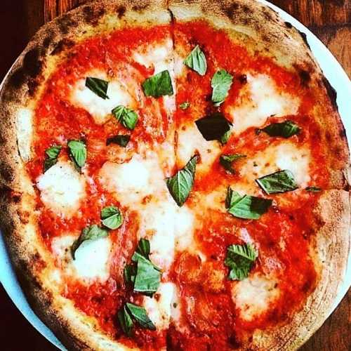 A freshly baked pizza topped with tomato sauce, mozzarella cheese, and fresh basil leaves on a wooden table.