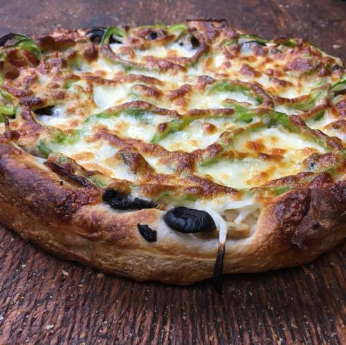 A freshly baked pizza topped with melted cheese, green peppers, and black olives on a wooden surface.
