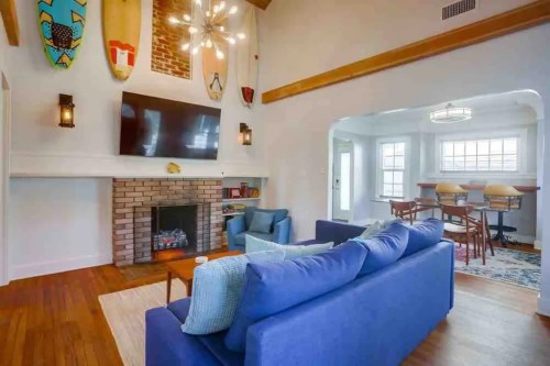Bright living room with blue sofa, brick fireplace, surfboards on the wall, and a dining area in the background.
