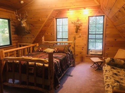 Cozy wooden cabin bedroom with a bed, rustic decor, and large windows letting in natural light.
