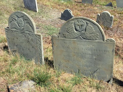 Two old gravestones in a grassy cemetery, one dedicated to Tabitha Longfellow, with decorative carvings and inscriptions.