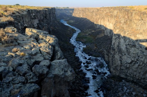 A winding river flows through a deep canyon with rocky cliffs and sparse vegetation under a clear sky.