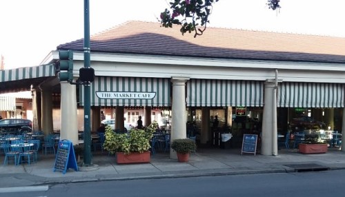 Exterior of The Market Café featuring striped awnings, outdoor seating, and potted plants along the entrance.