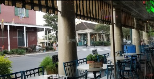 View from inside a restaurant, featuring tables and chairs, with a street and buildings visible outside.