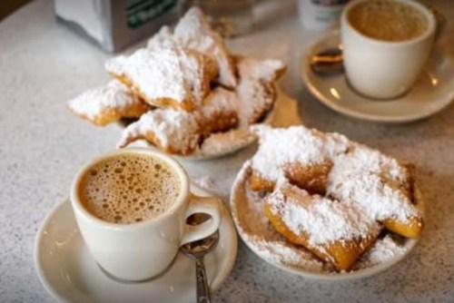 A plate of powdered sugar-covered beignets next to a cup of coffee on a table.