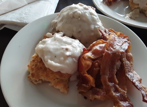 A plate with two biscuits topped with creamy gravy and crispy bacon strips on the side.