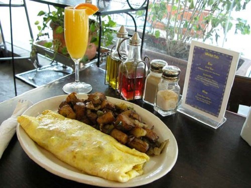 A plate with a cheese omelet and seasoned potatoes, accompanied by a mimosa and condiments on a table.