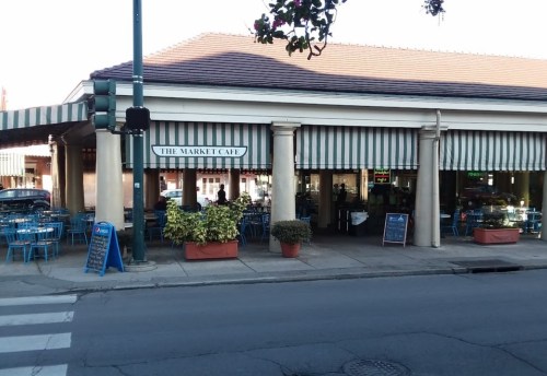 Exterior of The Market Café with striped awnings, outdoor seating, and potted plants, viewed from across the street.
