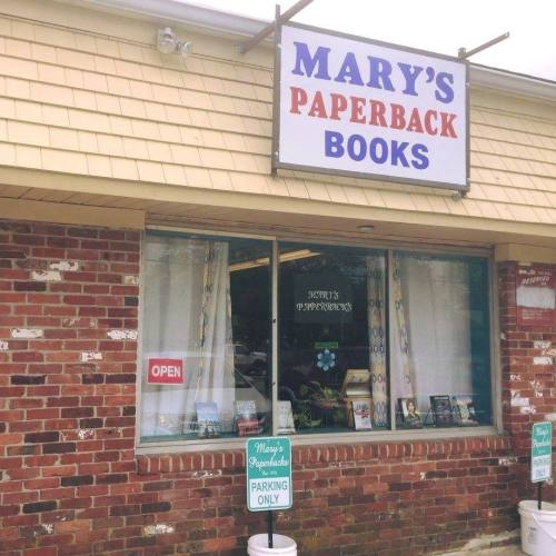 Sign for "Mary's Paperback Books" with an open sign in the window and parking signs outside.