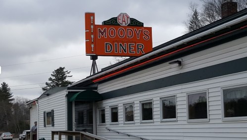 Sign for Moody's Diner on a cloudy day, featuring a classic diner exterior with a green awning and large windows.