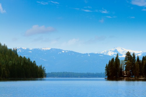 A serene lake surrounded by lush forests and snow-capped mountains under a clear blue sky.