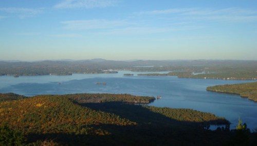 A panoramic view of a serene lake surrounded by lush green hills under a clear blue sky.