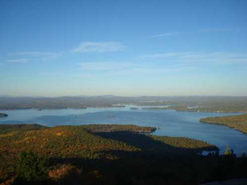 A scenic view of a lake surrounded by colorful autumn foliage and distant mountains under a clear blue sky.