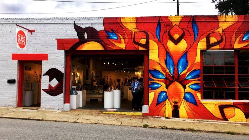 Colorful mural on a brick building with an open garage door, showcasing art inside and a person standing outside.