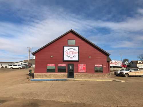 A red barn-style building with a sign reading "Next Door," featuring menus for salads and appetizers.