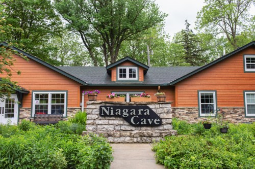 A rustic building with a stone sign reading "Niagara Cave," surrounded by greenery and trees.
