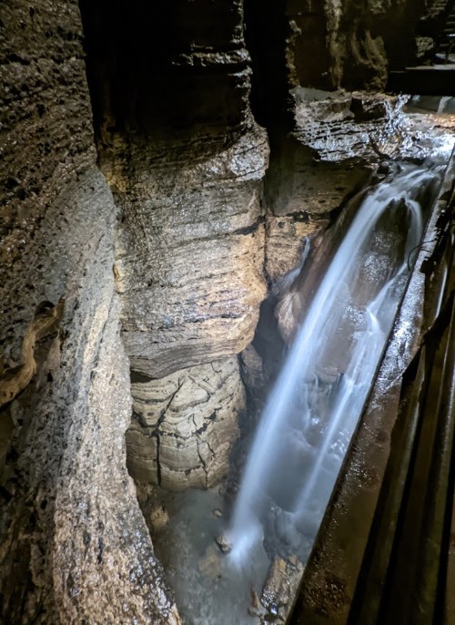 A waterfall cascades down rocky cliffs into a serene pool below, surrounded by textured stone walls.