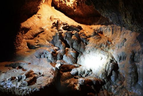 A dimly lit cave interior featuring textured rock formations and a small light illuminating the wet surface.