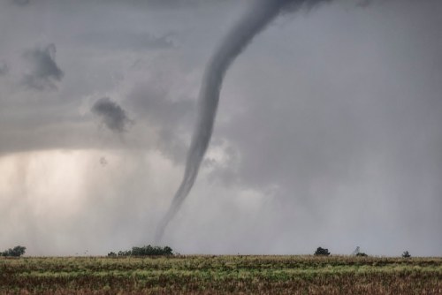 A dark tornado descends from a stormy sky over a flat landscape, with clouds swirling ominously above.