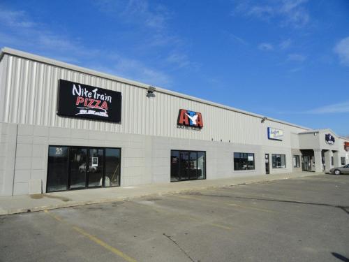 Exterior of a commercial building featuring Nite Train Pizza and other storefronts under a clear blue sky.