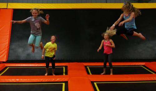 Four children are jumping on trampolines in a vibrant indoor trampoline park.