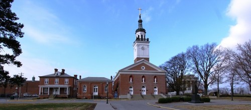 Historic brick church with a tall steeple, surrounded by trees and a clear blue sky.