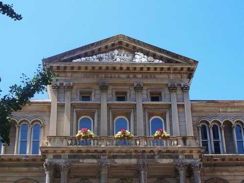 Historic building facade with ornate architecture, featuring columns, decorative sculptures, and flower-adorned balconies.