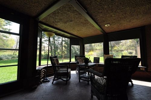 Cozy sunroom with wicker furniture, large windows, and a view of a green garden outside.
