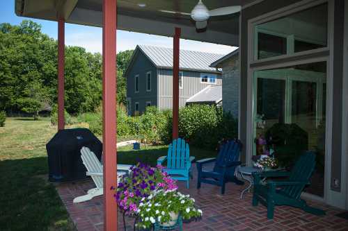 A cozy patio with colorful chairs and potted flowers, overlooking a garden and a modern house in the background.