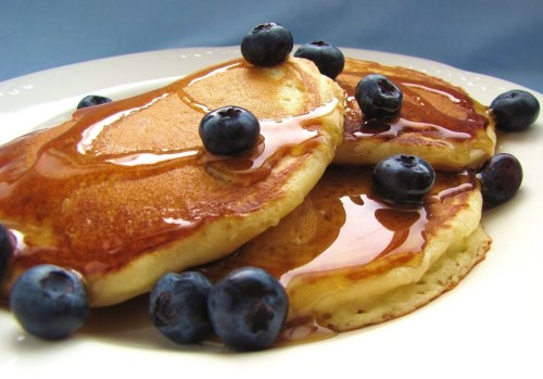 Two golden pancakes drizzled with syrup, topped with fresh blueberries, served on a white plate.