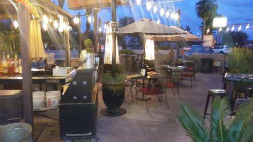 Outdoor dining area with tables, umbrellas, and string lights, set against a twilight sky.