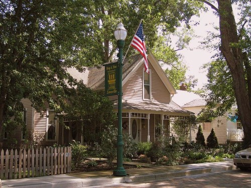 A charming house with a front porch, surrounded by trees and a white picket fence, featuring an American flag.