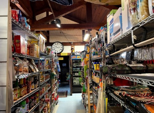 A view of a grocery store aisle lined with shelves of various products, featuring a clock on the wall.