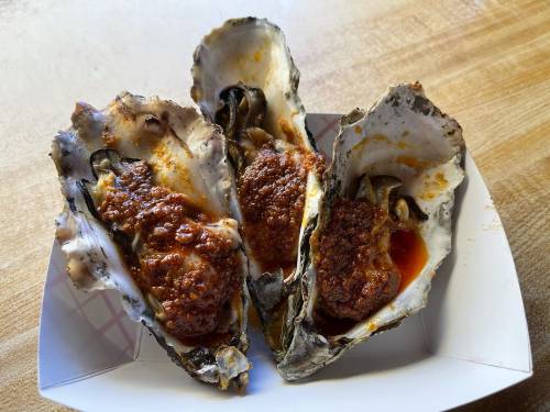 Three baked oysters topped with a savory sauce, served in their shells on a white plate.