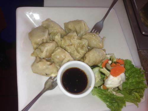Plate of dumplings served with a small bowl of dipping sauce and a side salad of lettuce and vegetables.