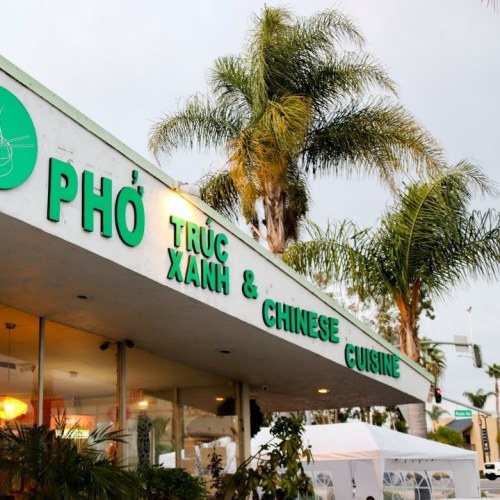 Exterior of a restaurant named "Phở Trúc Xanh & Chinese Cuisine," featuring palm trees and a cloudy sky.