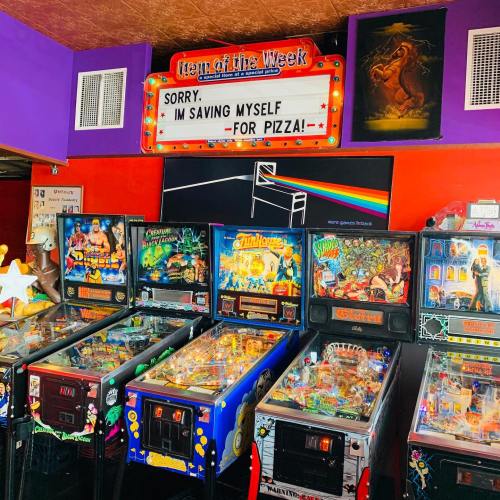 A colorful arcade with several pinball machines and a sign that reads, "Sorry, I'm saving myself for pizza!"
