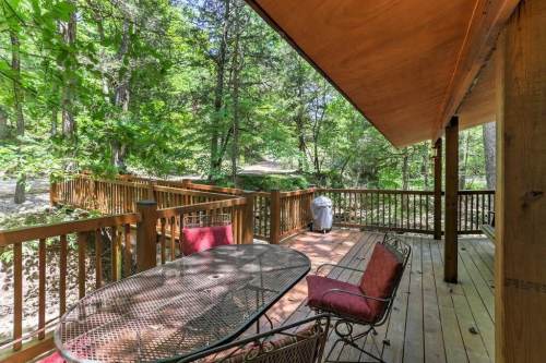 A wooden deck with a table and chairs, surrounded by lush greenery and trees.