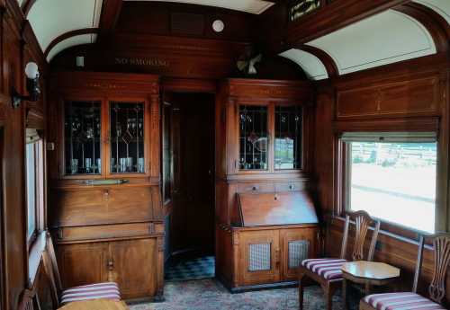 Interior of a vintage train car featuring wooden paneling, a "No Smoking" sign, and elegant furnishings.