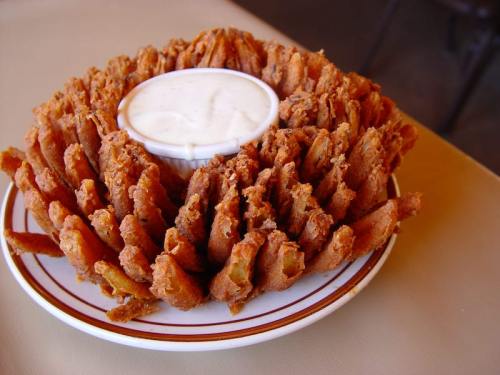 A large, crispy onion blossom served on a plate with a small bowl of dipping sauce in the center.