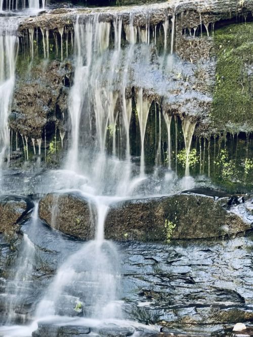 A serene waterfall cascading over rocky terrain, with water flowing gently and greenery surrounding the scene.