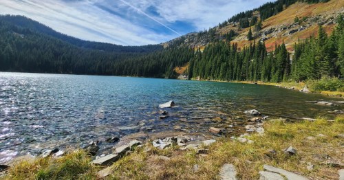 A turquoise lake is surrounded by steep mountains and tall pine trees in northern Idaho.