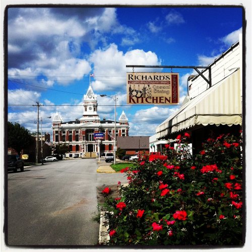 A street view featuring Richard's Kitchen sign, colorful flowers, and a historic building with a clock tower in the background.